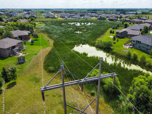 Drone view showing a high voltage power line cutting across a grassed wetland in a residential district. photo