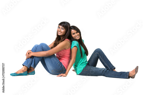 Cheerful young Indian friends sitting with back to each other on floor.