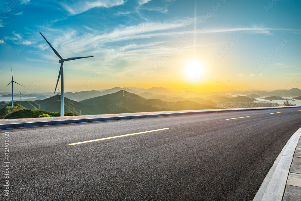 Asphalt highway and wind turbines with mountain natural landscape at sunset. High Angle view. - obrazy, fototapety, plakaty 