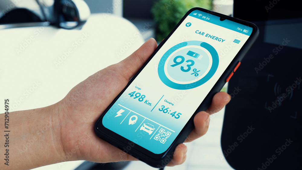 Smartphone display battery status on smart EV mobile application while EV car recharging electricity by home charging station in garage. Future innovative EV car and energy sustainability. Peruse