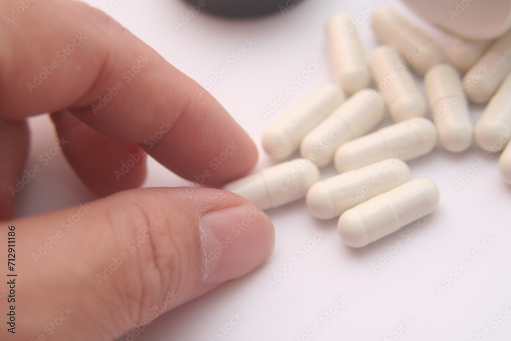 close up of hand holding white capsules on white background with copy space close up of hand holding white capsules on white background with copy space