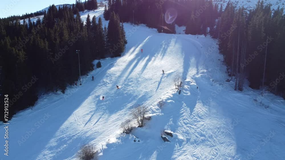 Static aerial clip of people skiing round the bend of a mountain slope in the sunshine at Vitosha ski resort near Sofia, Bulgaria with a chairlift running in the background