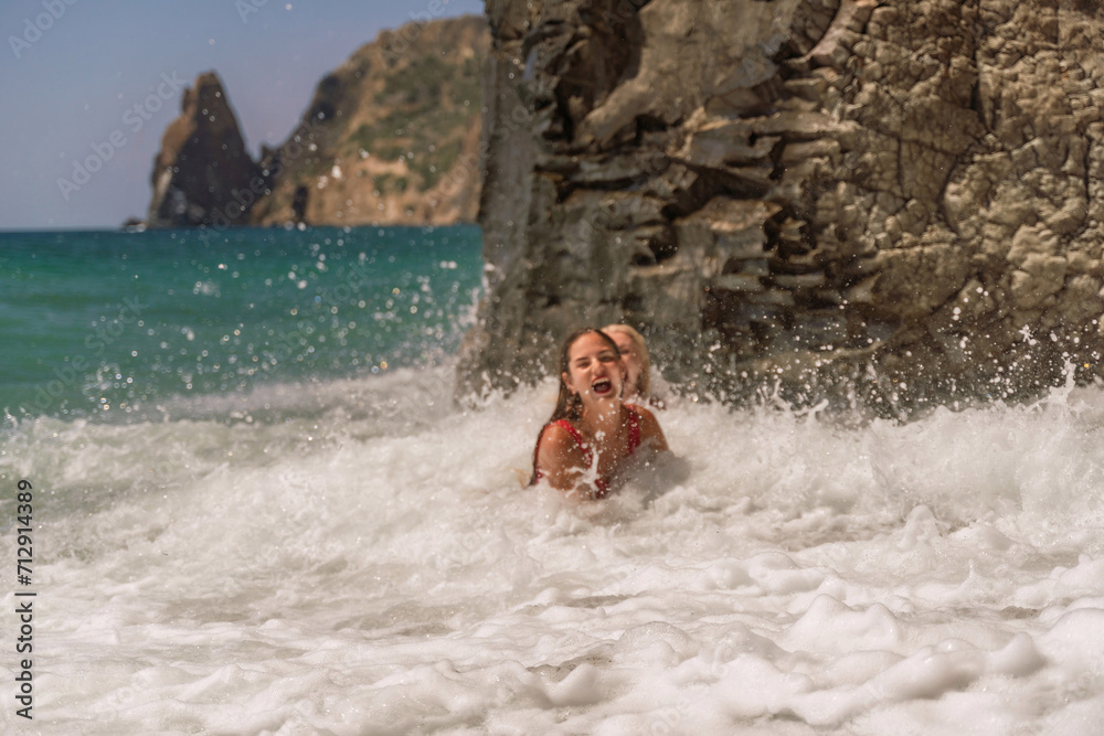 Fototapeta premium Women ocean play. Seaside, beach daytime, enjoying beach fun. Two women in red swimsuits enjoying themselves in the ocean waves.