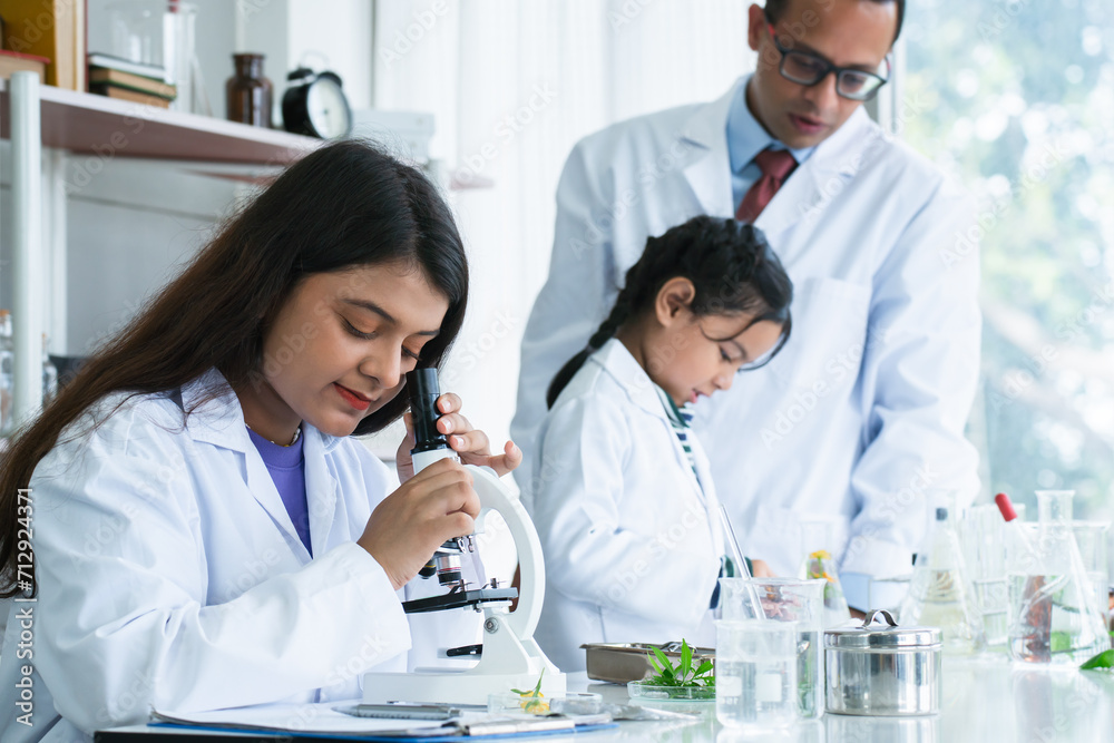 Indian scientist woman student using microscope do an experiment at biology class in school laboratory while teacher teaching another kid student. Education, science and school concept Indian scientist woman student using microscope do an experiment at biology class in school laboratory while teacher teaching another kid student. Education, science and school concept