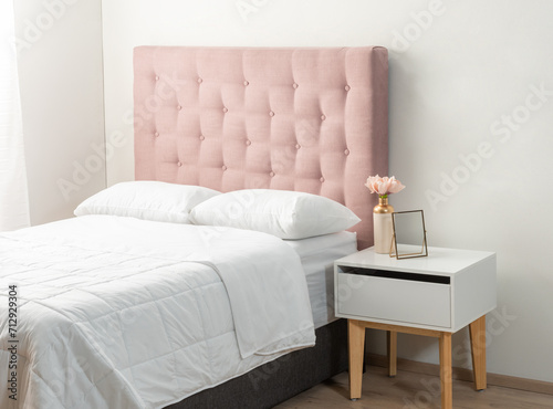 Sophisticated Feminine Bedroom: Plush Pink Tufted Headboard Sets a Delicate Tone, Matched by a Modern White Nightstand with Wooden Legs, Accented by a Pastel Bloom in a Gold Vase.