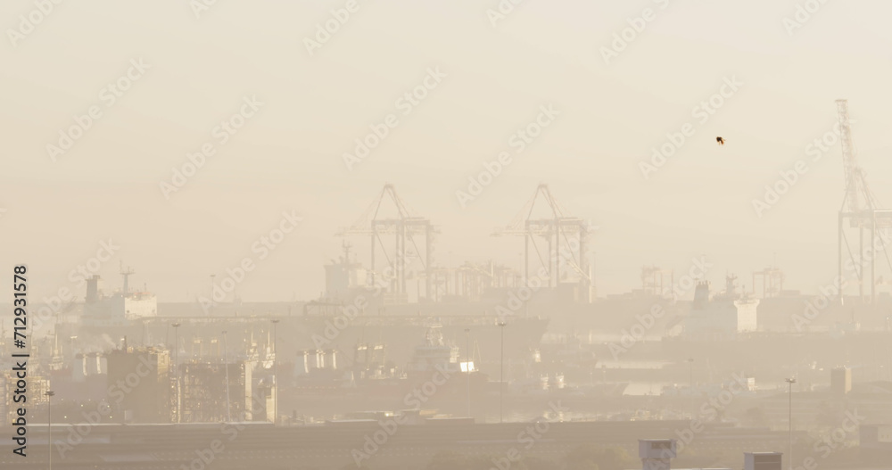 A hazy view of a port with cranes and ships, with copy space