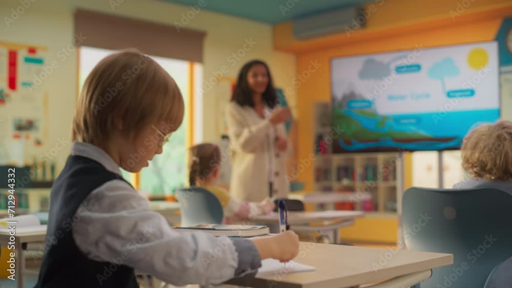 Curious Smart Boy Writing Down Notes in His Notebook During a Primary School Geography Class. Young Enthusiastic Female Teacher Explaining the Laws of Water Circulation in Nature with a Presentation Curious Smart Boy Writing Down Notes in His Notebook During a Primary School Geography Class. Young Enthusiastic Female Teacher Explaining the Laws of Water Circulation in Nature with a Presentation