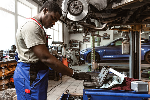 African male auto-mechanic repairing car brakes under the car in auto service