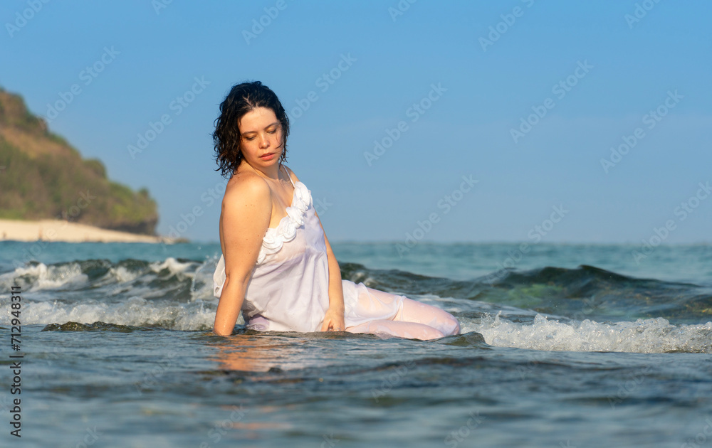 Beautiful woman in white dress sits in the water on ocean shores Beautiful woman in white dress sits in the water on ocean shores
