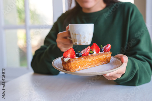 Closeup image of a woman holding a plate of mix berry log croissant and coffee cup