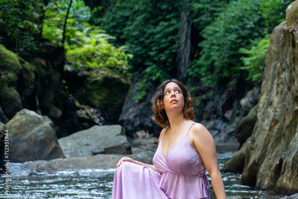 A young woman in beautiful pink dress rests on the banks of the river and rainforest. A young woman in beautiful pink dress rests on the banks of the river and rainforest.