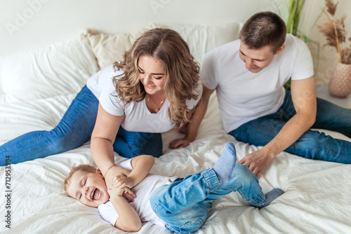 Happy parents tickling son in bright bedroom and laughing photo