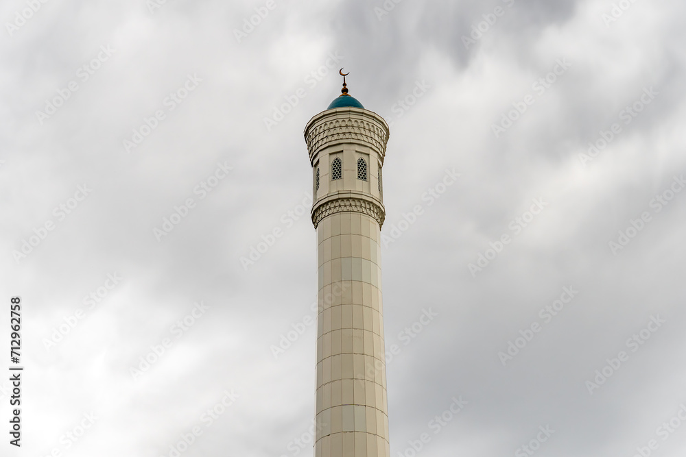 Beautiful high minaret made of white stone against a sky with clouds. Islam and Muslim traditions and religion. Concept of faith and religious buildings. Beautiful high minaret made of white stone against a sky with clouds. Islam and Muslim traditions and religion. Concept of faith and religious buildings.