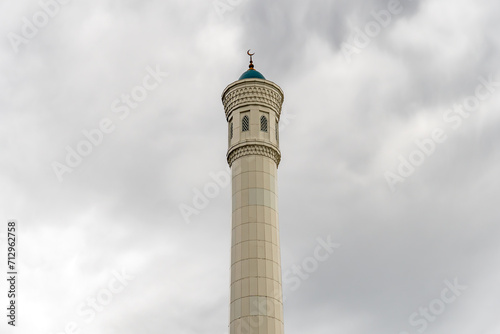 Beautiful high minaret made of white stone against a sky with clouds. Islam and Muslim traditions and religion. Concept of faith and religious buildings.