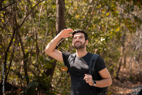 Happy Caucasian man carrying backpack traveling spends free time hiking, walking, exploring, adventure in forest beautiful autumn day, enjoying nature amidst mountains and trees during the weekend.