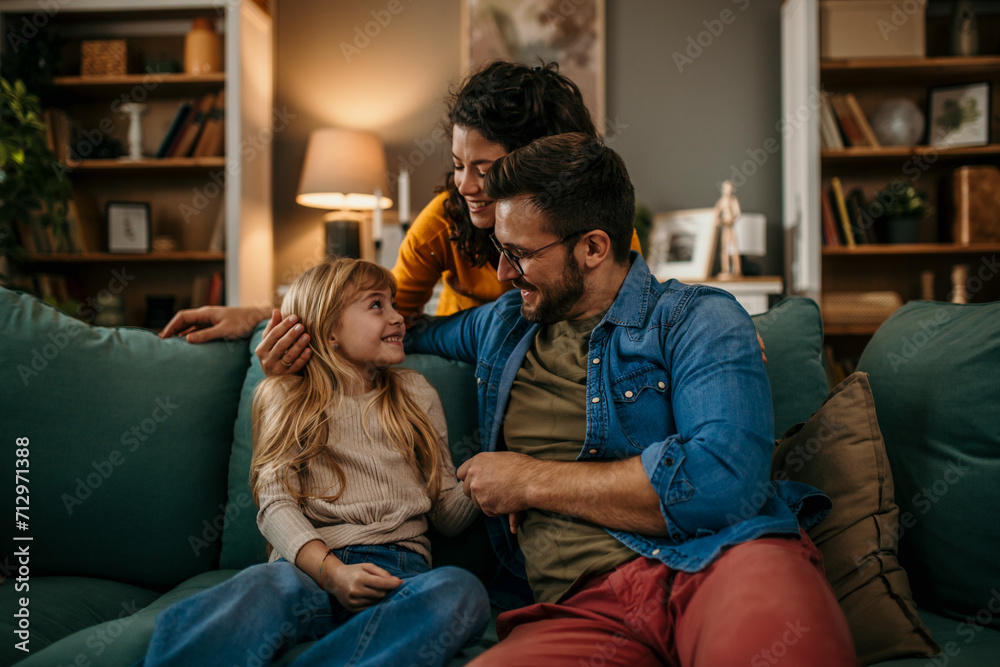 Parents and their daughter sharing laughter and conversation on the living room sofa