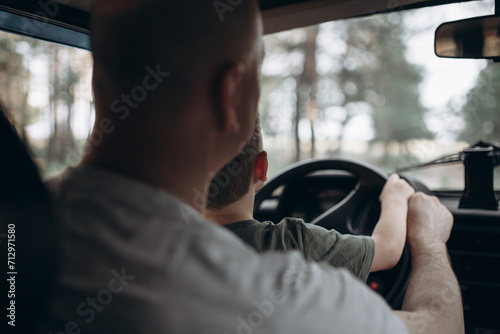 Dad teaches his son to drive a car view from the back