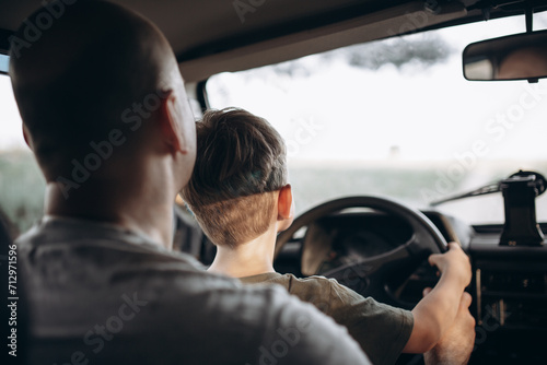 Dad teaches his son to drive a car view from the back
