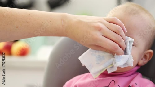 A mother's hand wipes snot from the nose of a little boy aged one year old who is sneezing and has a cold. Infection and viruses, close-up. Snot bubbles