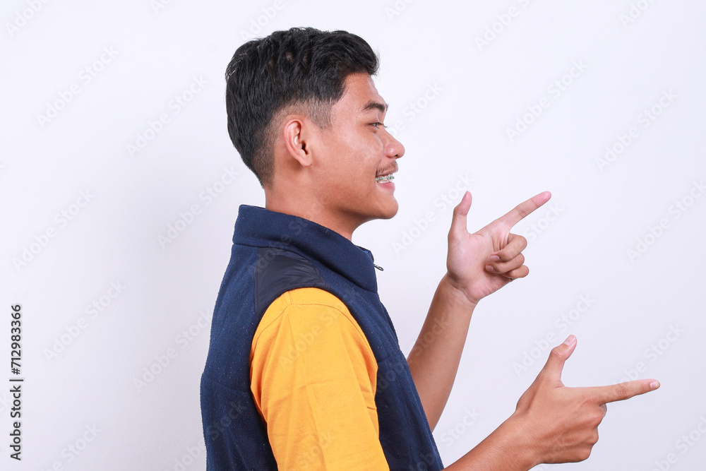 Side view of happy smiling Asian guy with dental braces pointing fingers, showing its you gesture, standing over white background Side view of happy smiling Asian guy with dental braces pointing fingers, showing its you gesture, standing over white background