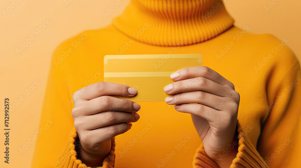 Close-up of hands holding a golden credit card on a yellow backdrop. - obrazy, fototapety, plakaty 