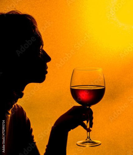 Drinking of red wine at the sunset. Silhouette of woman holding a glass of red wine her hand hand.