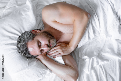 Man sleeping in bed. Top view of handsome man sleeping in bed. Morning healthy sleep. Guy sleeping on bed in bedroom. Middle aged adult man is sleeping at home. Cozy bed, white pillow mattress.