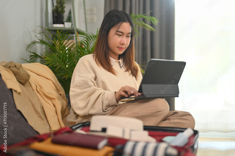 Young woman planning for trip with digital tablet, getting ready for holidays travel trip in living room Young woman planning for trip with digital tablet, getting ready for holidays travel trip in living room