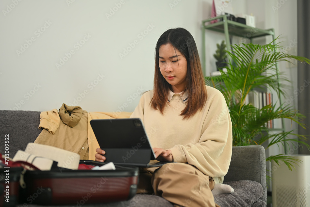 Young woman planning for trip with digital tablet, getting ready for a vacation in living room Young woman planning for trip with digital tablet, getting ready for a vacation in living room