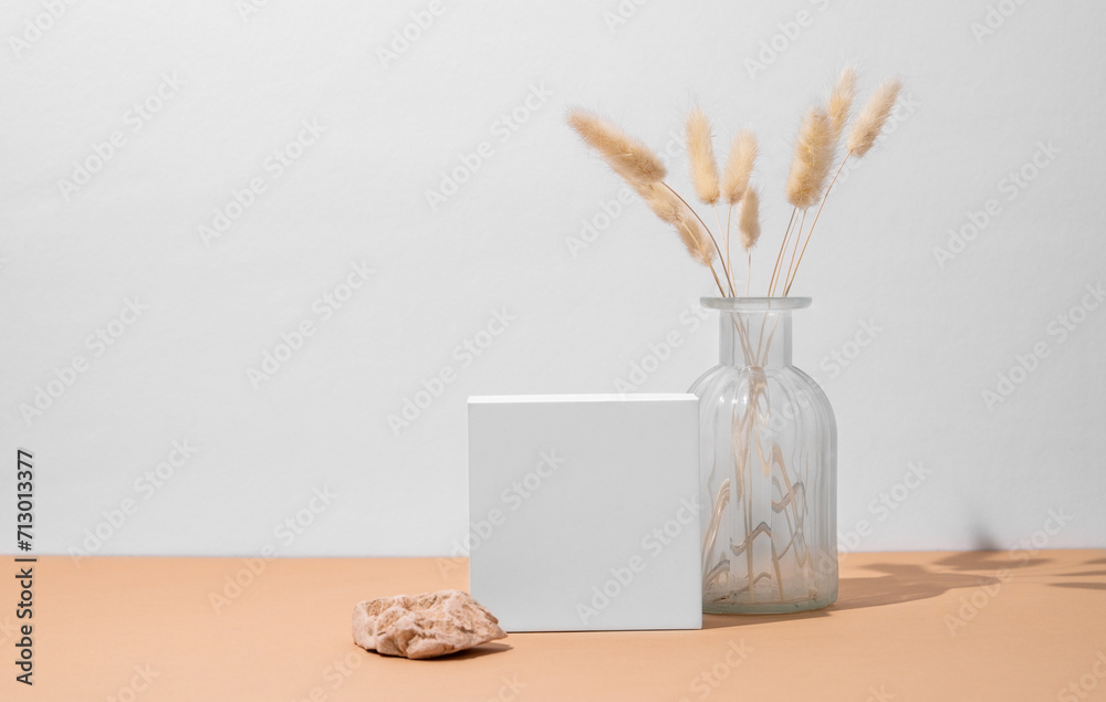 White empty box and vase with dried flowers on a beige background with a hard shadow.