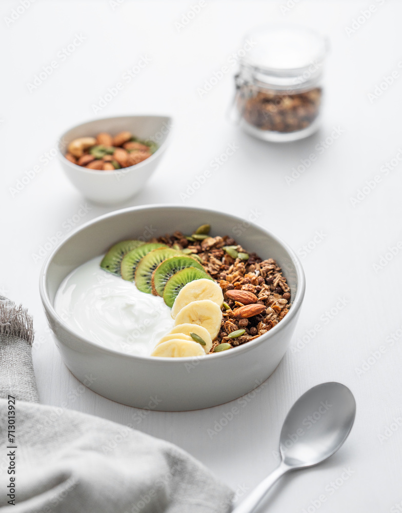 Granola with banana and kiwi on a white table with a spoon and napkin.