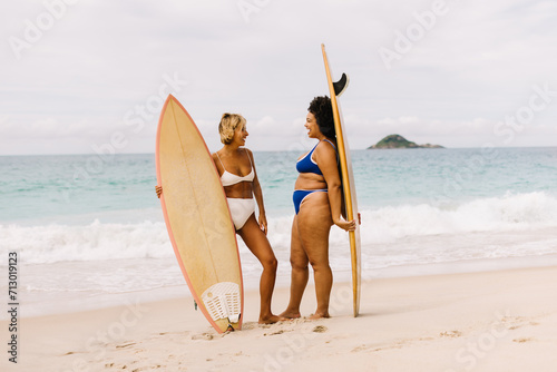 Surfing adventure for two: Female surfers standing on the beach in bikinis