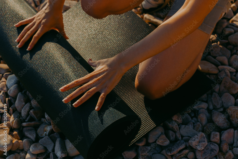 Woman unrolling black yoga mat on rocks. Close-up of hands on mat