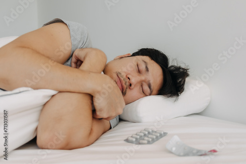 Asian man get sick, get cuddly, sleeping with medicines on white bed, resting alone in apartment.