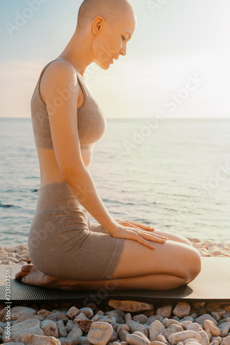 Bald woman practicing on yoga mat with sea background at sunset