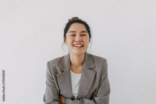 Happy Asian Thai woman smiling laughing and looking at camera, businesswoman crossing arms, wearing blazer suit and bun hairstyle, successful at work, standing isolated over white background wall.