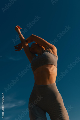 Fotografie Slender woman in gray yoga suit poses against blue sky.