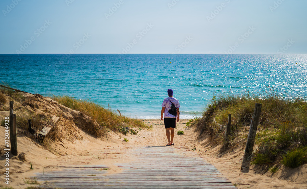 man strolling along wooden path on the beach