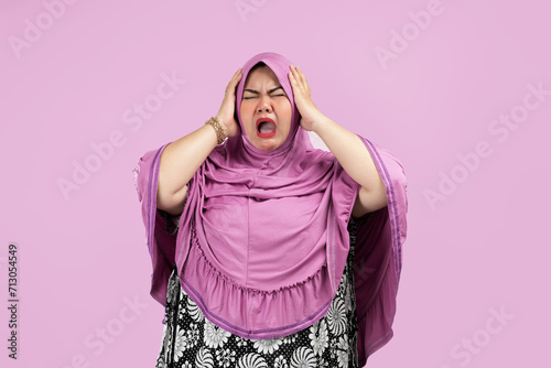 Asian Muslim women with shocked facial expressions and holding her heads Wearing a pink hijab. isolated on a pink background