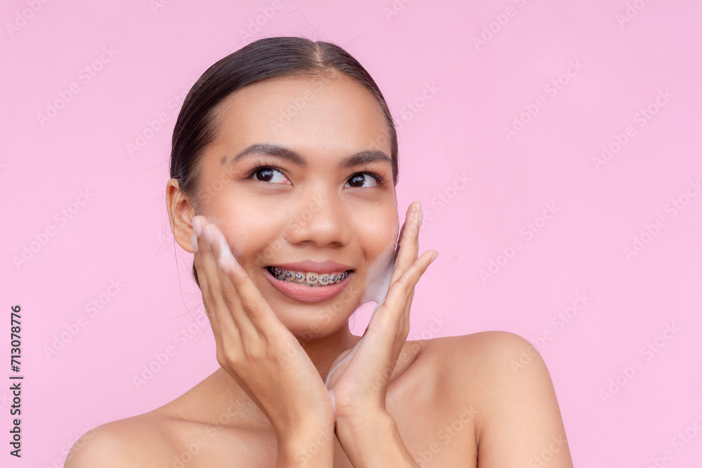 A young pretty filipino lady using facial foam wash for her cheeks and face. Soft pink background. A young pretty filipino lady using facial foam wash for her cheeks and face. Soft pink background.