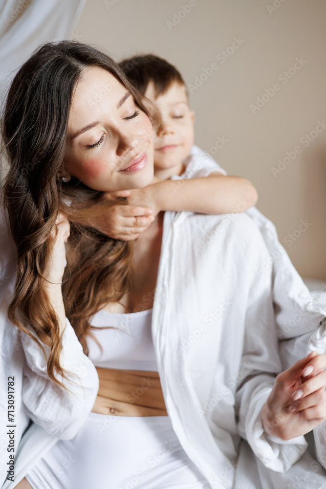 Blurred toddler boy hugging mother in shirt on bed at home Blurred toddler boy hugging mother in shirt on bed at home