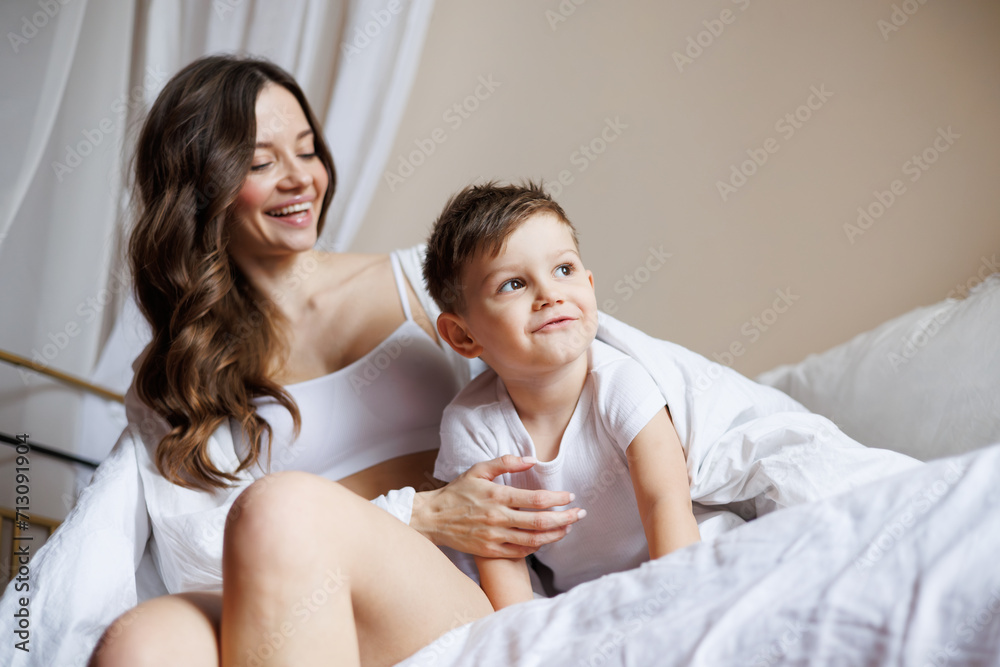 Cheerful mother hugging cute toddler son on bed in morning at home Cheerful mother hugging cute toddler son on bed in morning at home