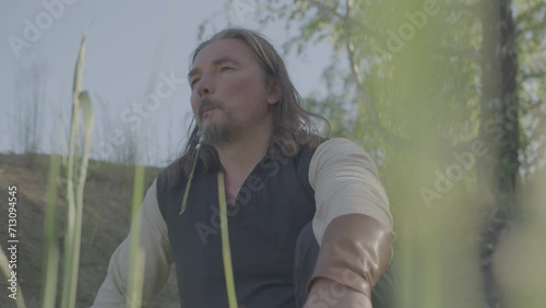 A man in medieval peasant clothing rests under a tree.