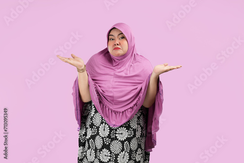 Fat Asian Muslim women open up their hands and look Confused about a choice. Wearing pink hijab. isolated on a pink background