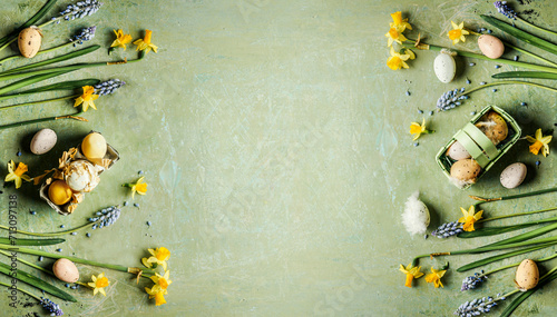 Green Easter background with springtime flowers and Easter eggs, top view. Frame