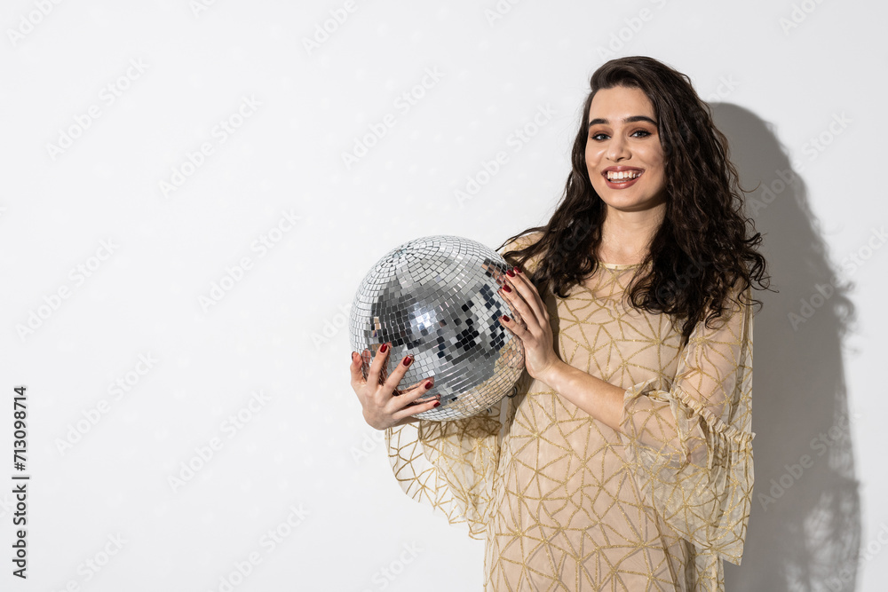 Naklejka premium Happy young woman wearing dress smiling is holding disco ball. Party concept