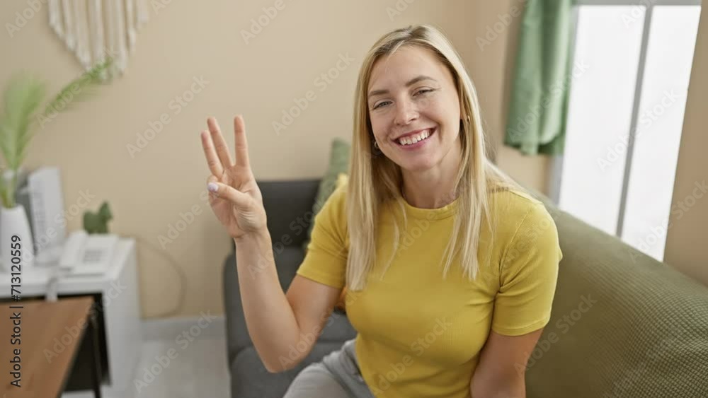 Cheerful young blonde woman confidently showing number three, joyfully pointing fingers up indoors Cheerful young blonde woman confidently showing number three, joyfully pointing fingers up indoors