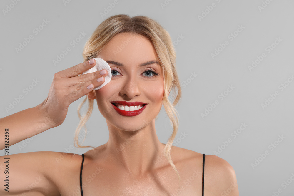 Smiling woman removing makeup with cotton pad on light grey background. Space for text Smiling woman removing makeup with cotton pad on light grey background. Space for text