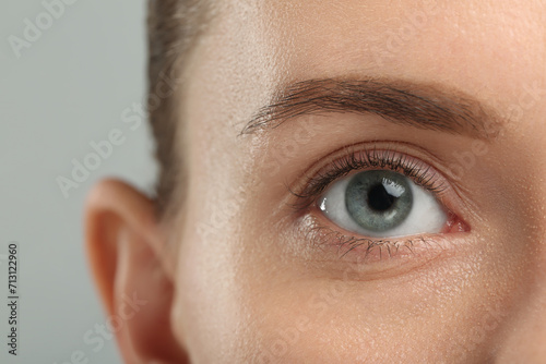 Woman with beautiful natural eyelashes on grey background, closeup