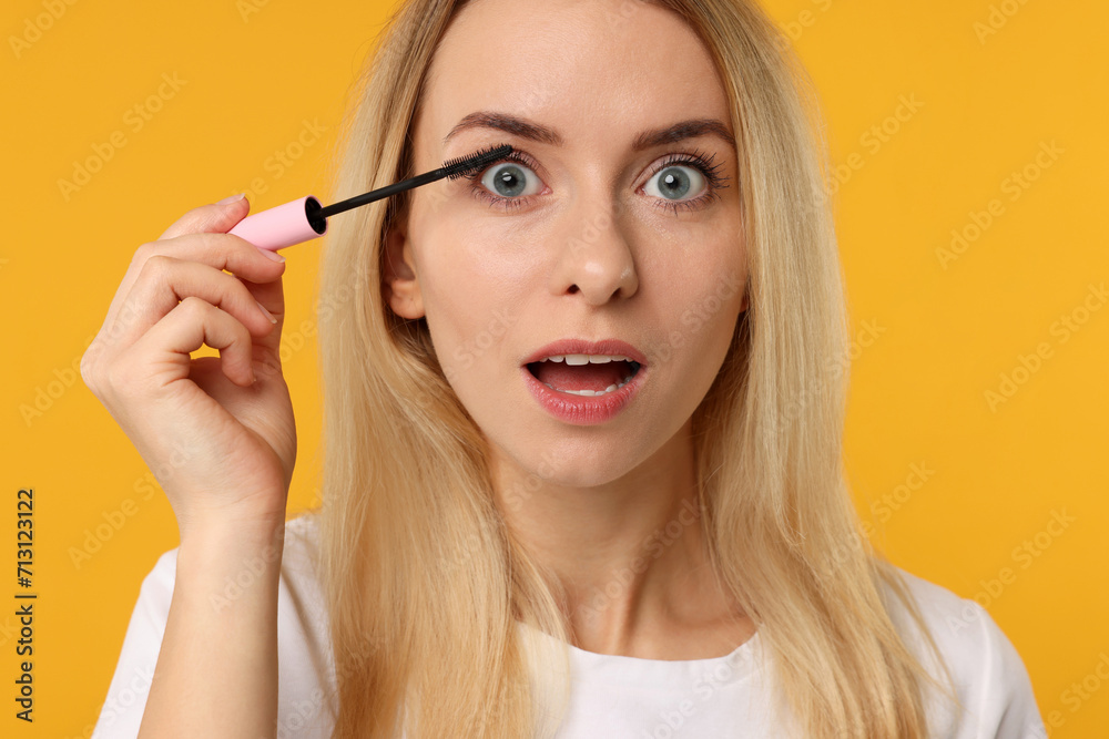 Beautiful woman applying mascara on orange background, closeup Beautiful woman applying mascara on orange background, closeup